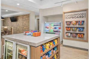 A snack bar area with a refrigerated display, a beverage cooler, and shelves stocked with snacks. - Candlewood Suites Newnan - Atlanta SW by IHG (Newnan)