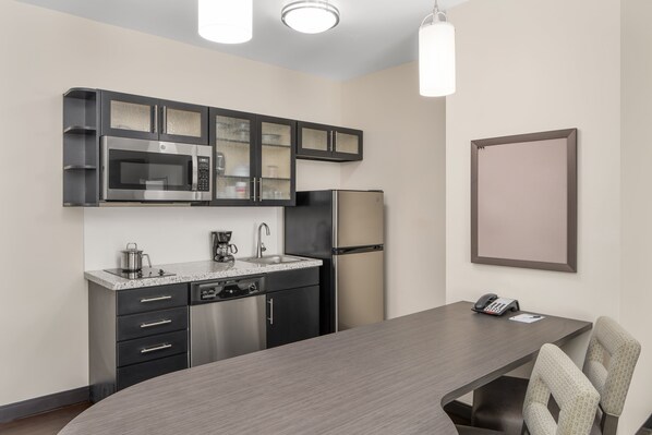 A modern kitchen with a microwave, stove, refrigerator, and a dining area with a table and chairs. - Candlewood Suites Newnan - Atlanta SW by IHG (Newnan)