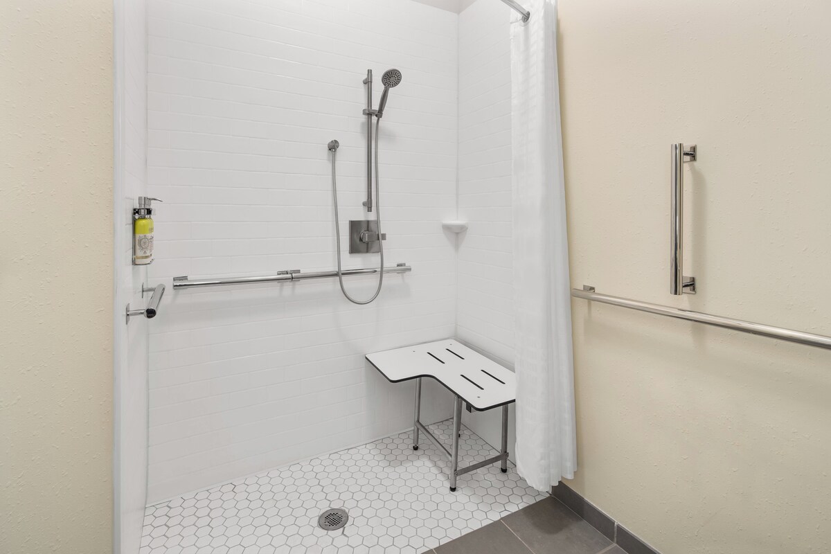 A wheelchair-accessible shower stall with a grab bar, a white tiled floor, and a small bench.