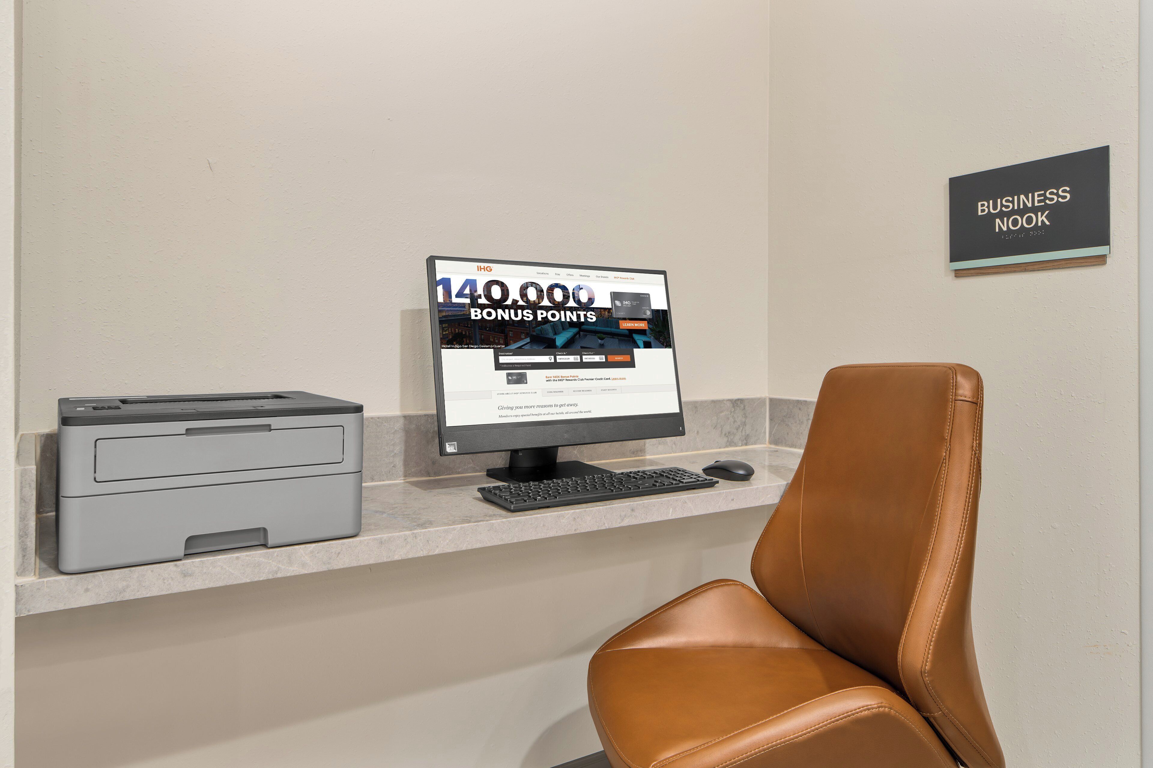 Ein Computermonitor zeigt ein Hotel-Treueprogramm, ein Drucker und ein Ledersessel in einer Business-Lounge.