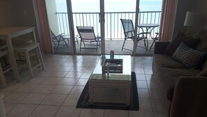 A living room with a glass coffee table, a sofa, and a balcony with chairs. - Steps Away from the Soft, White, Sandy Beaches of Beautiful Marco Island!! (Marco Island)