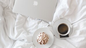 A laptop, a cup of coffee, and a plate of dessert on a bed. - Hotel-Events Adlerpalast (Ruesselsheim)