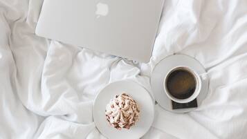 A laptop, a cup of coffee, and a plate of dessert on a bed.