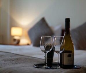 A bed with two wine glasses and a bottle of wine on a table.