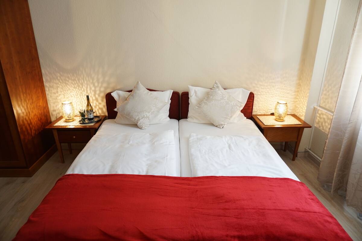 Un lit double avec une couvre-lit rouge, deux oreillers blancs et deux tables de chevet avec des lampes.