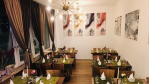 A restaurant with multiple tables set for dining, featuring green tablecloths, white napkins, and candles. - Hotel-Events Adlerpalast (Ruesselsheim)