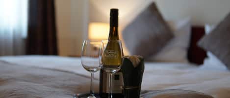A bed with a bottle of wine and two glasses on it.