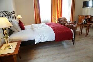 Un lit bien fait, avec une literie blanche et rouge, une lampe de chevet et une table de nuit en bois.