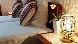 A neatly made bed with striped pillows, a bedside table with a decorative lamp, and a potted orchid. - Hotel-Events Adlerpalast (Ruesselsheim)