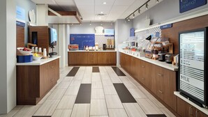 Ein moderner Frühstücksbereich mit einer zentralen Theke, Vitrinen und Schildern, die Bereiche wie 'Express Start Frühstück' und 'Bäckerei' kennzeichnen.