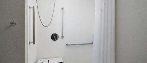 Ett modernt badrum med dusch, stödhandtag och en vit tvättställ.