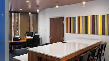 A modern conference room with a large table, chairs, a computer desk with a monitor, and a colorful striped wall.