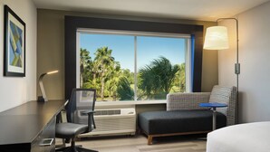 A hotel room with a desk, chair, and a view of palm trees through a large window. - Holiday Inn Express & Suites Brunswick by IHG (Brunswick)