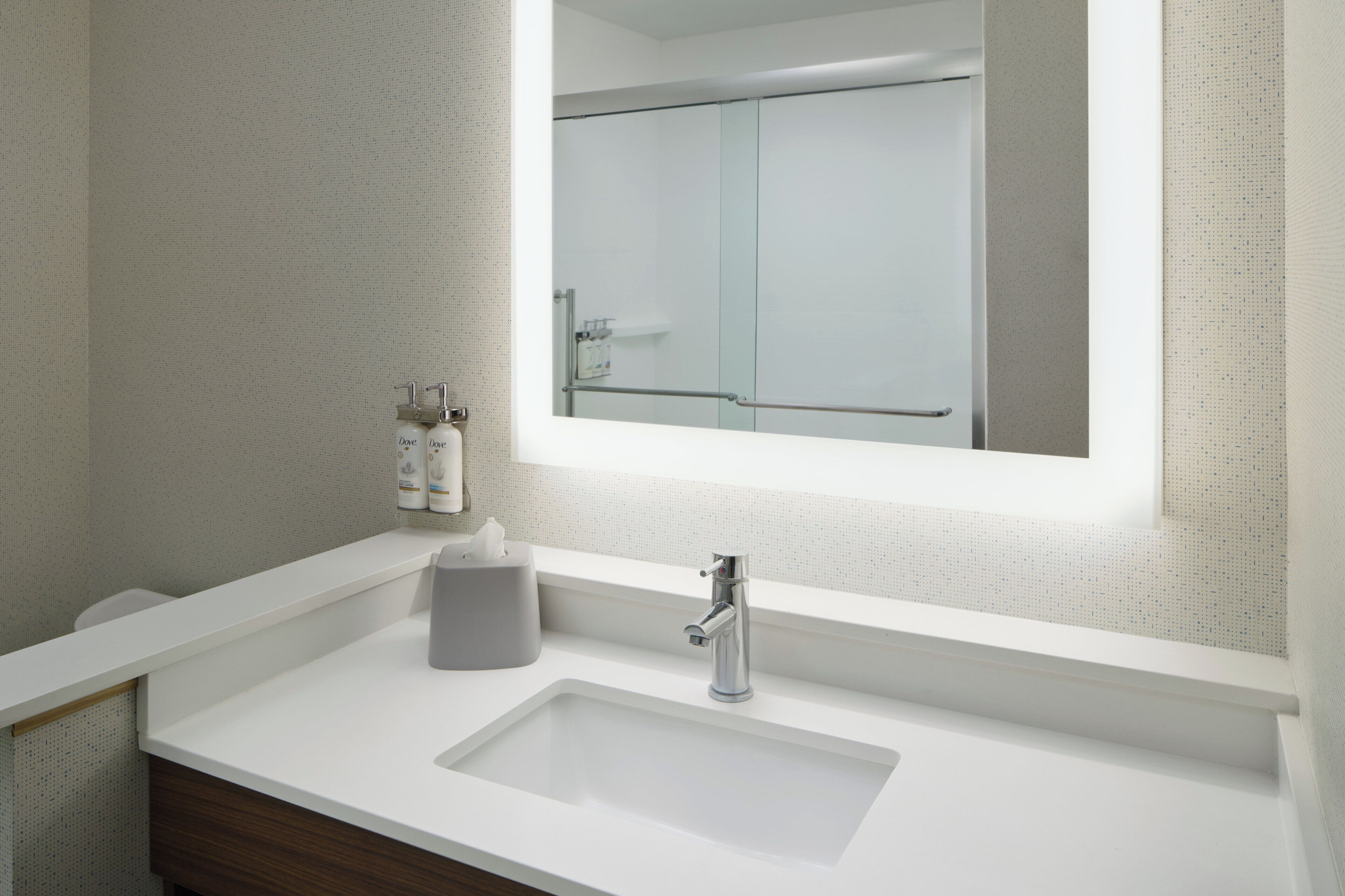 A modern bathroom with a white sink, a mirror, and a glass shower door.