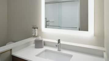 A modern bathroom with a white sink, a mirror, and a glass shower door.