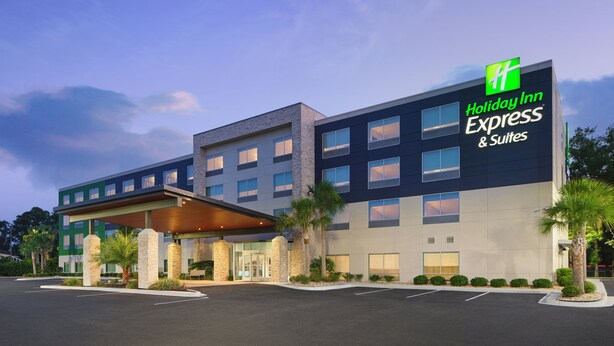 Ein Holiday Inn Express & Suites Gebäude mit modernem Design, das einen markanten Eingang und einen überdachten Bereich mit Palmen zeigt.