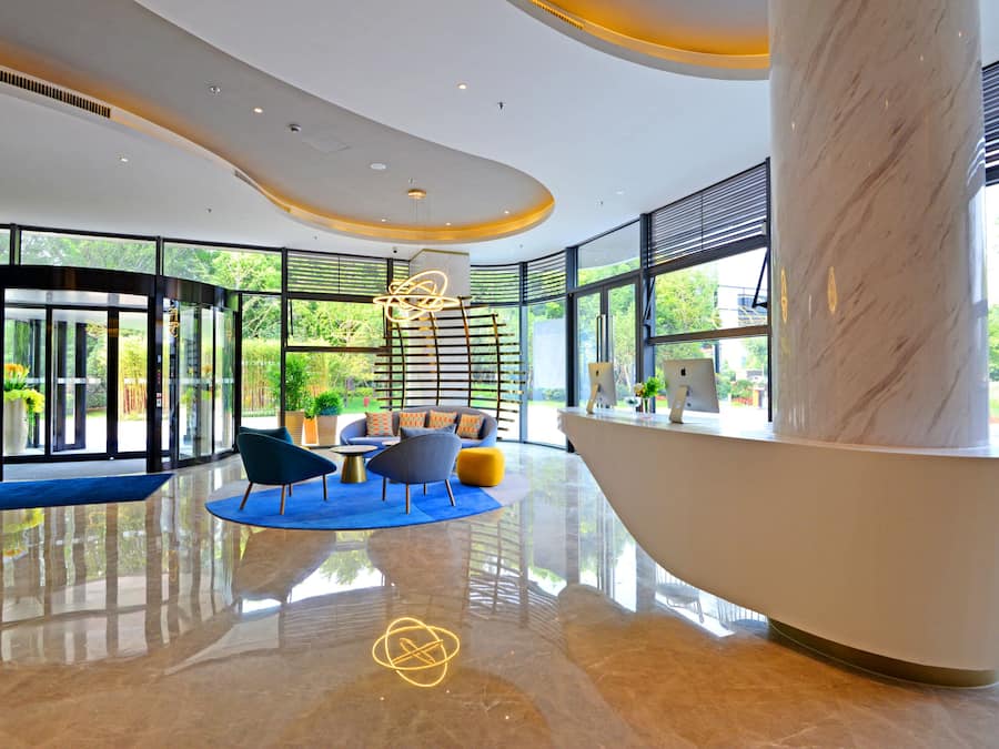 A modern lobby with a large marble column, curved ceiling, and seating area with a glass wall offering a view of greenery.
