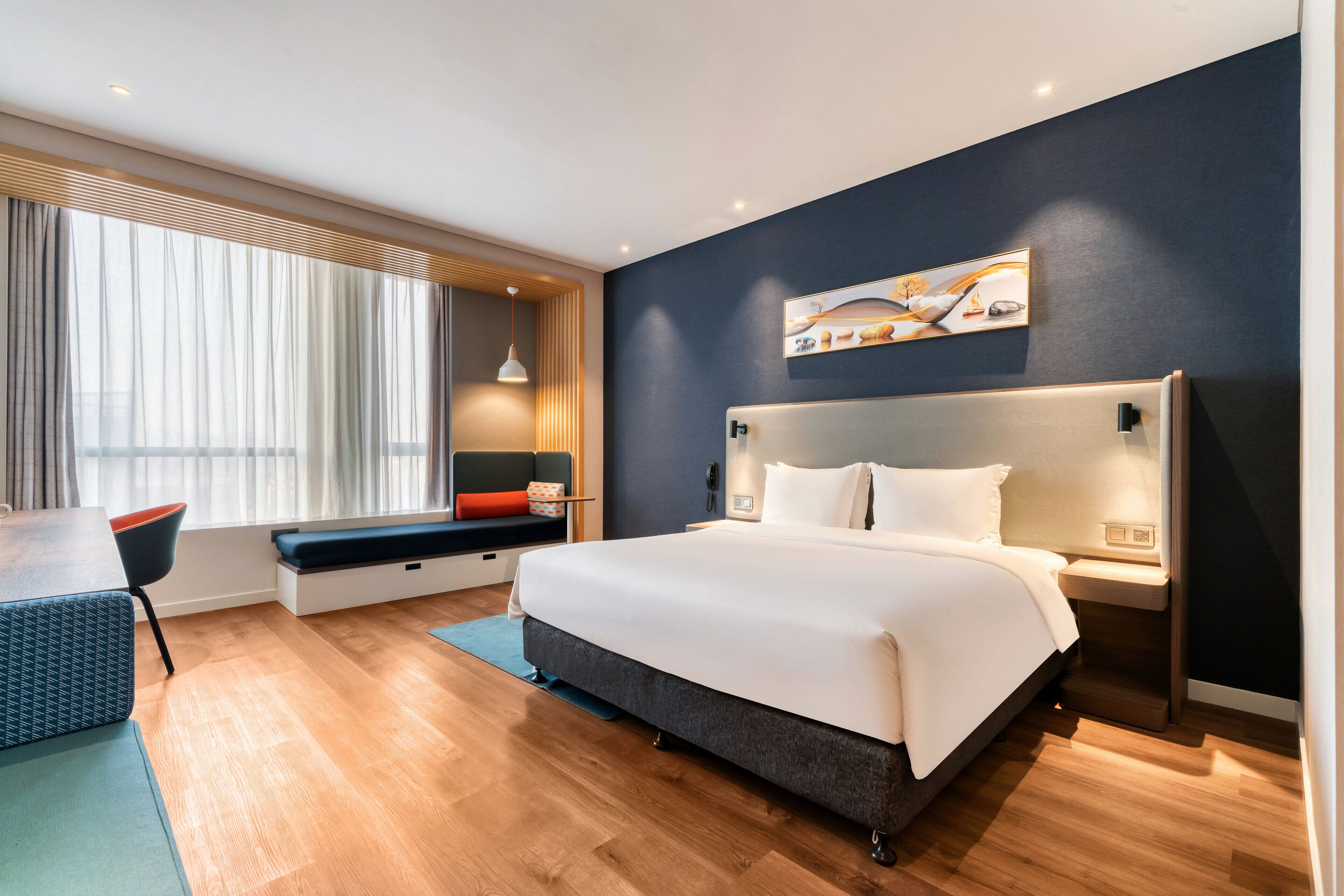 A modern hotel room with a large bed, a desk, and a seating area by the window.