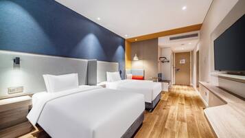 A hotel room with two beds, a TV, a desk, and a wooden floor.