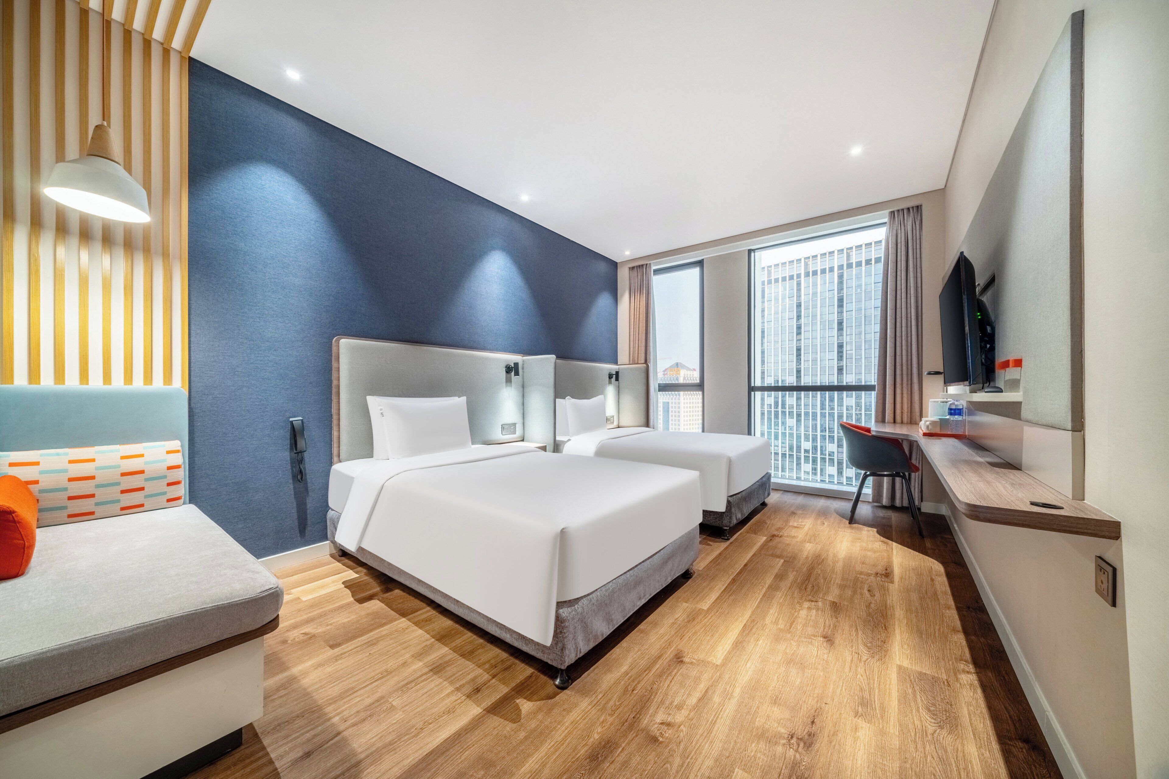 Une chambre d’hôtel avec deux lits, un bureau, une chaise, une télévision et une grande fenêtre.