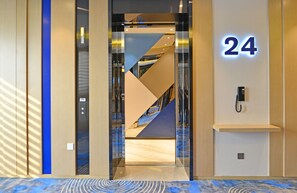 An interior view of a hotel entrance with a modern design, including a glass elevator, a number '24' sign, and a phone on the wall. - Holiday Inn Express Hangzhou Binjiang by IHG (Hangzhou)