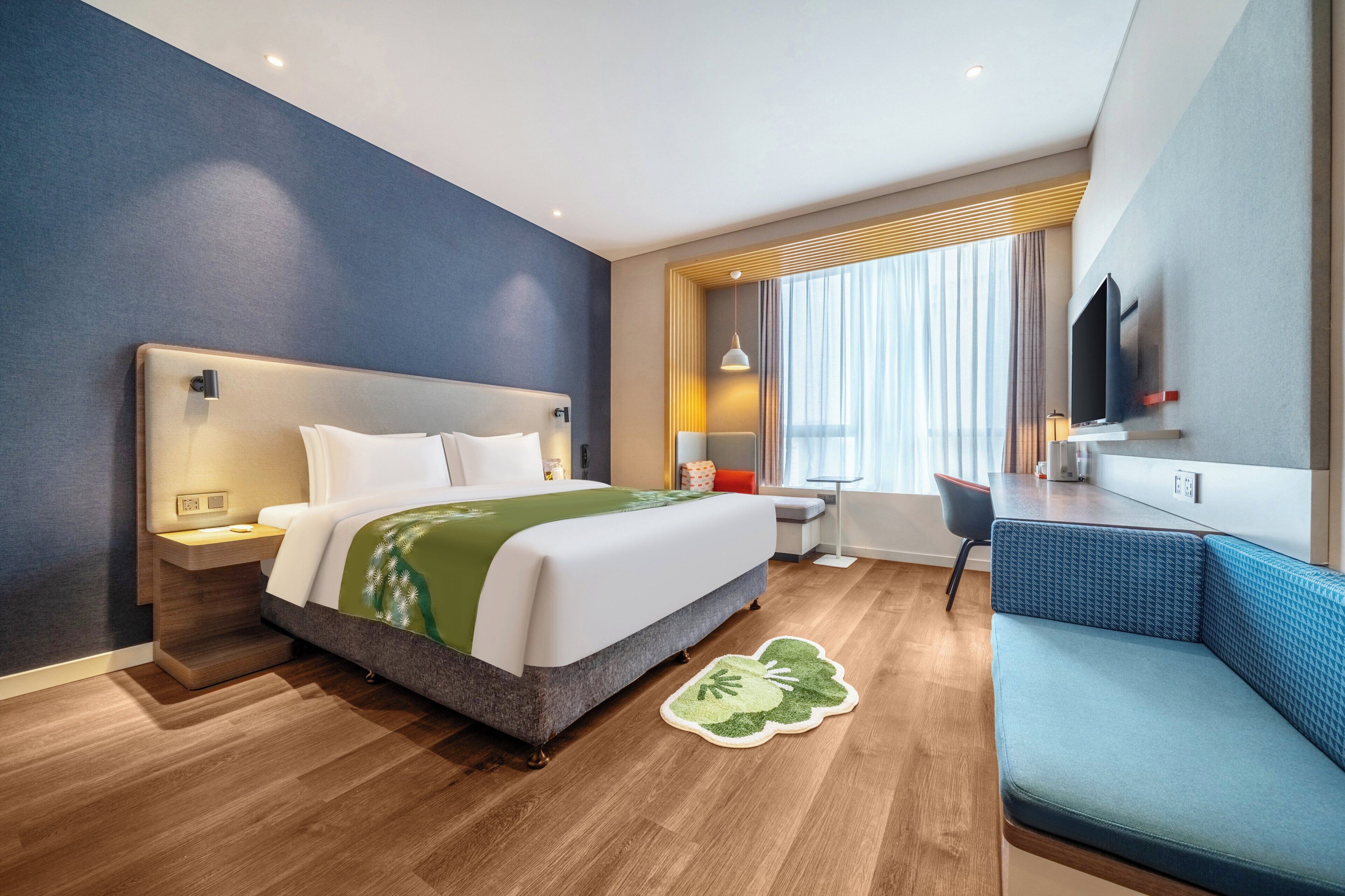A hotel room with a bed, bedside table, desk, chair, and a TV mounted on the wall.