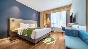 A hotel room with a bed, bedside table, desk, chair, and a TV mounted on the wall.