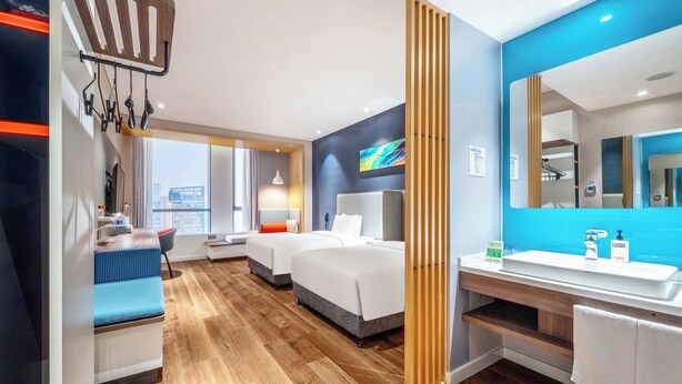 A modern hotel room with a large bed, a desk, a chair, a bathroom with a sink and mirror, and a view of the city. - Holiday Inn Express Hangzhou Binjiang by IHG (Hangzhou)