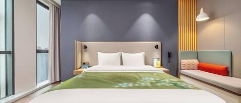 Una habitación de hotel moderna con una cama grande, mesitas de noche, un banco y vistas a la ciudad.
