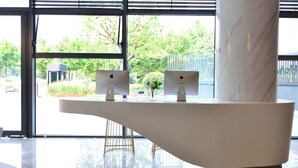 A reception desk with two monitors, a vase with flowers, and a view of greenery outside.
