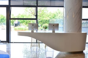 A reception desk with two monitors, a vase with flowers, and a view of greenery outside.