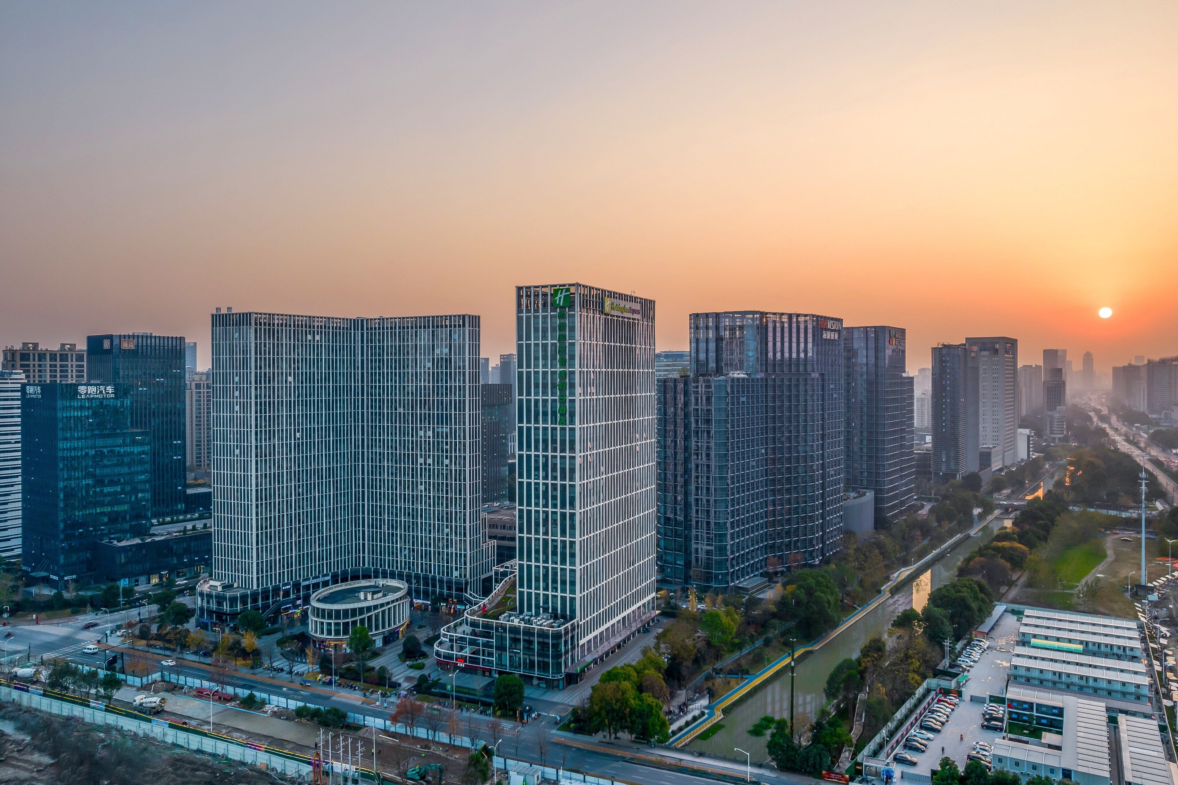 A high-rise urban building complex with multiple skyscrapers, a central tower with a grid-like facade, and a surrounding area with roads and greenery.