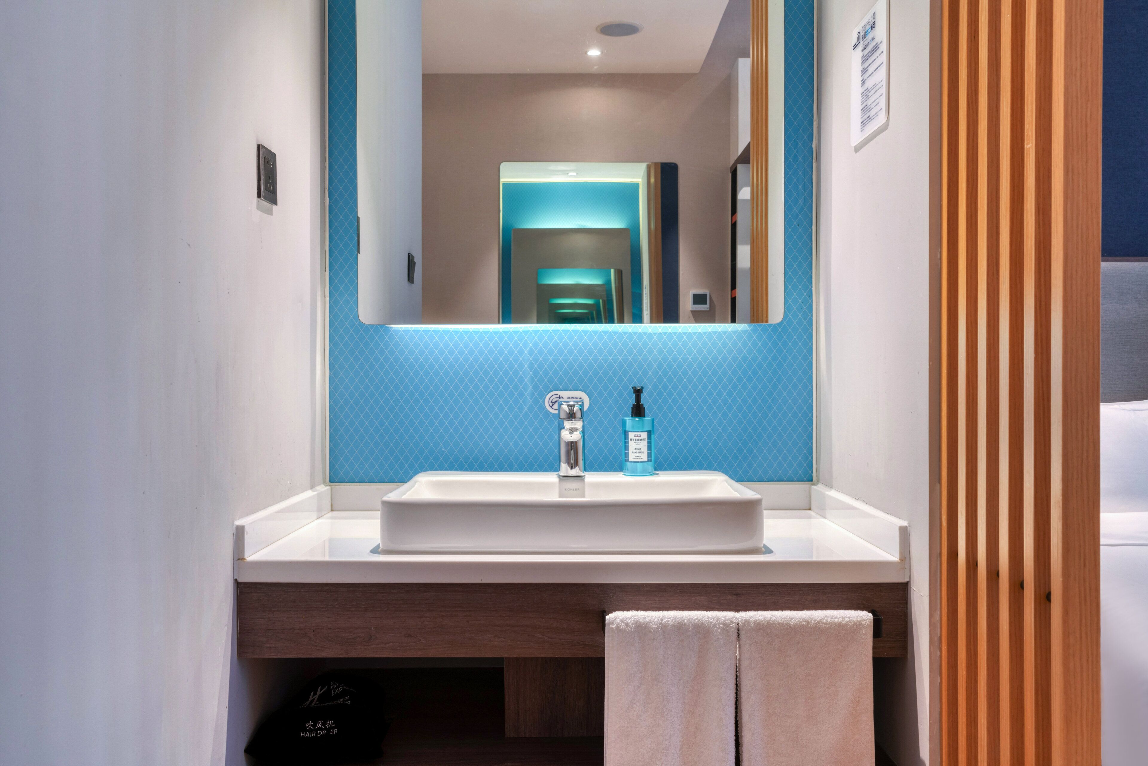 Een moderne badkamer met een witte wastafel, een blauwe accentmuur en een houten paneel aan de rechterkant.