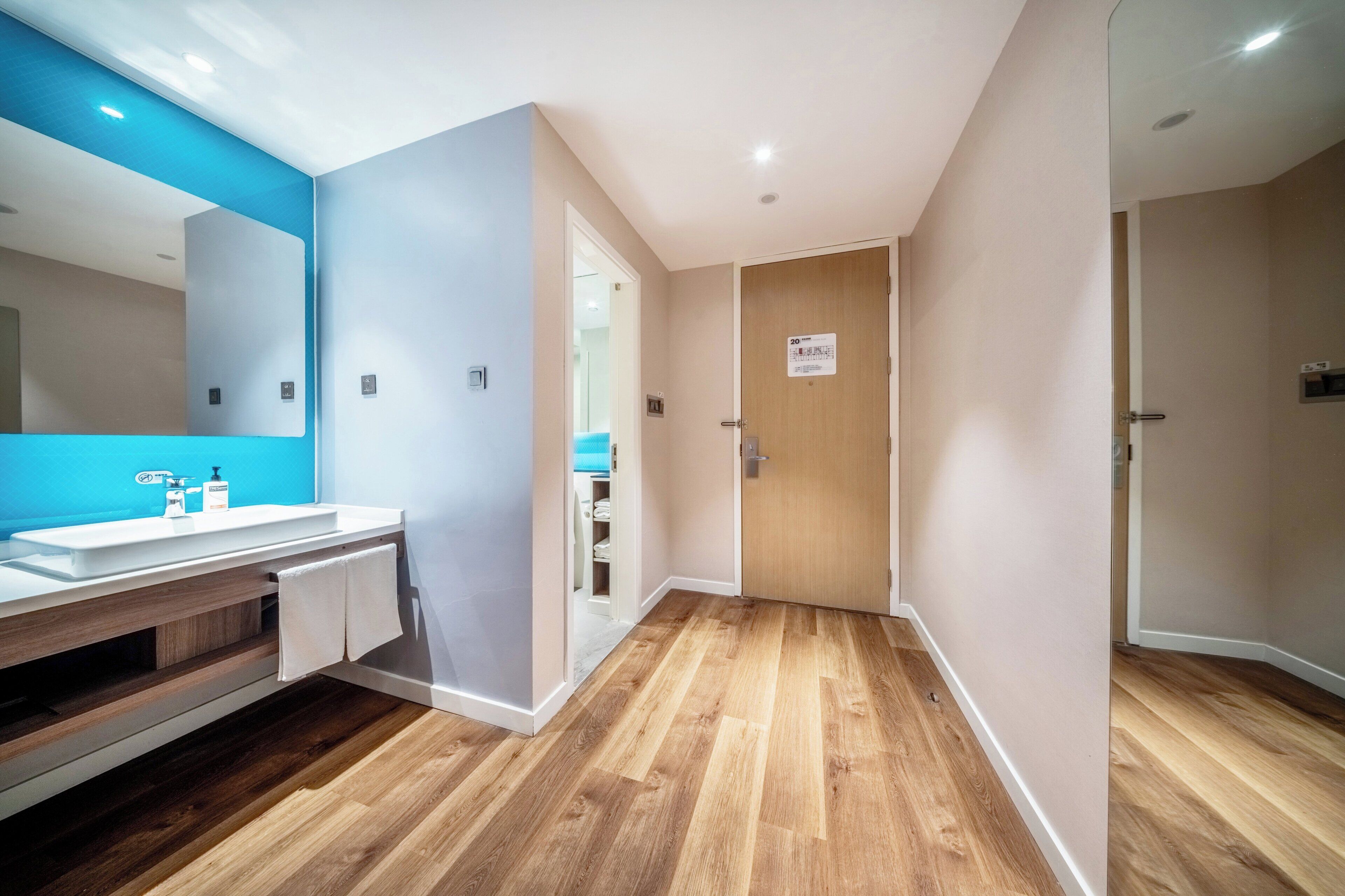 A modern bathroom with a wooden vanity, a large mirror, and a blue accent wall.