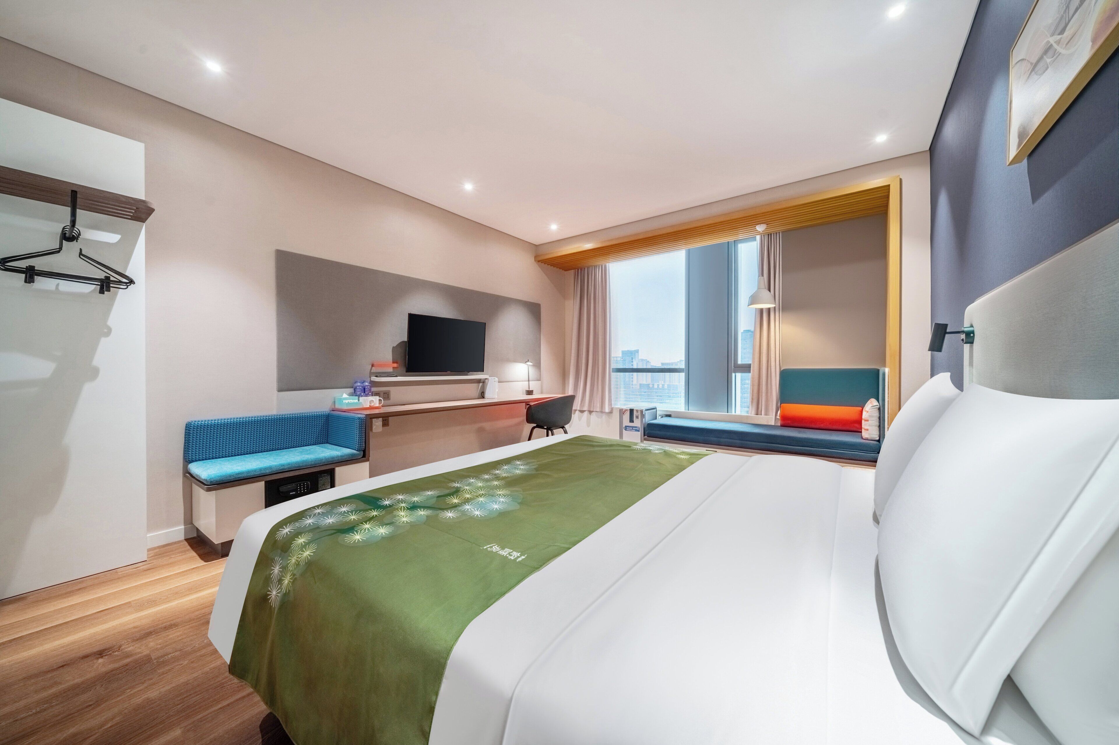 Habitación de hotel con cama, escritorio, silla, televisor y ventana con vista a la ciudad.