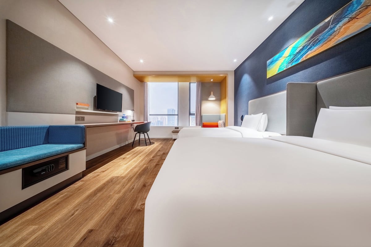 A hotel room with a bed, a sofa, a desk, a TV, and a large window.