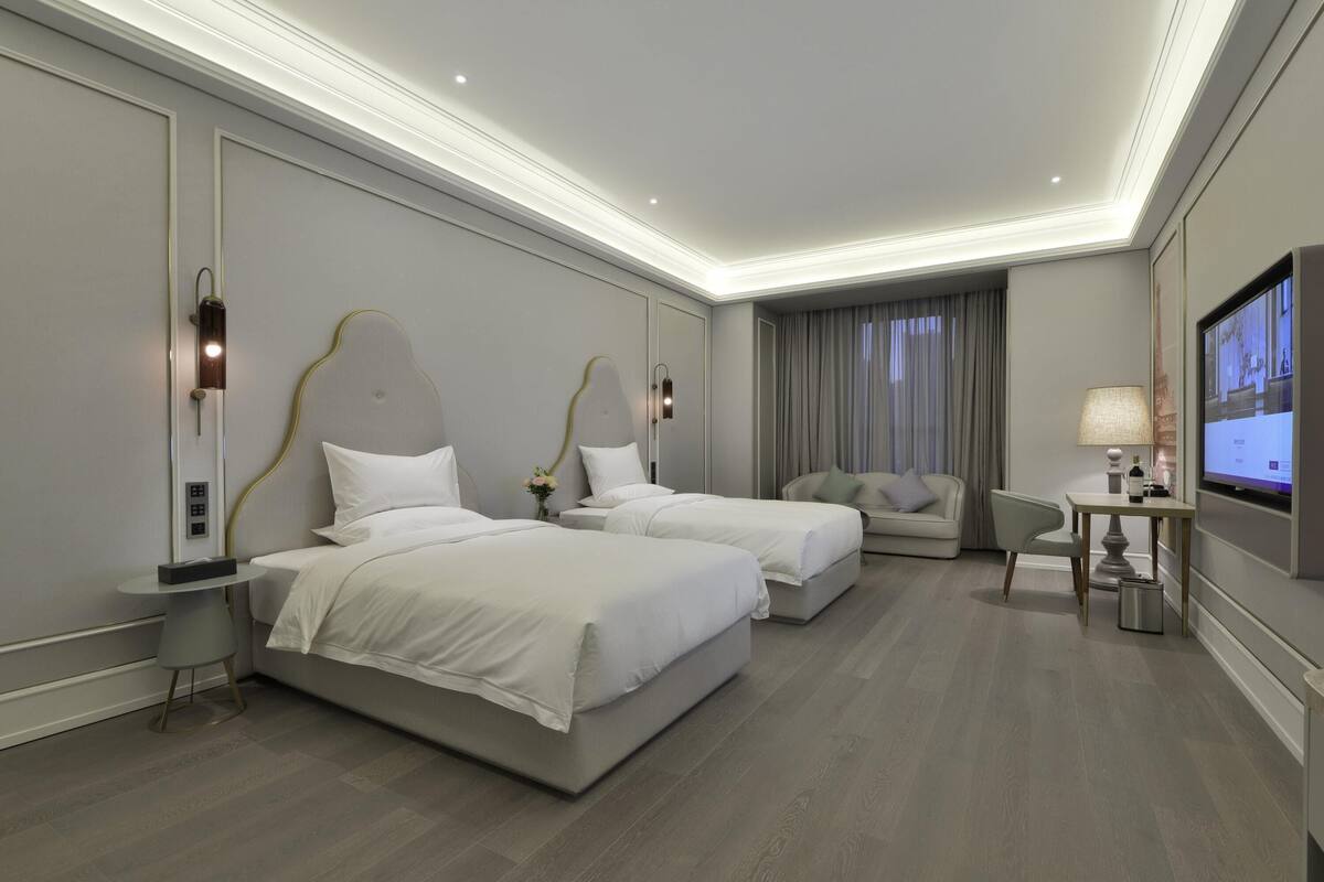 Une chambre d’hôtel avec deux lits, un canapé, une télévision et une lampe.