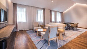 A modern hotel room with a wooden floor, a large window with curtains, a sofa set, a dining table with chairs, and a TV mounted on the wall. - Holiday Inn Express Guizhou Qinglong by IHG (Qianxinan Buyei and Miao)