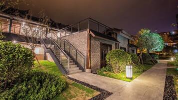 Un edificio moderno con una escalera que conduce a un segundo piso, rodeado de follaje cuidado y un camino pavimentado.