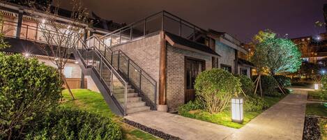 Un bâtiment moderne doté d’un escalier menant à un deuxième étage, entouré d’un espace verdoyant bien entretenu et d’un chemin piétonnier dallé.