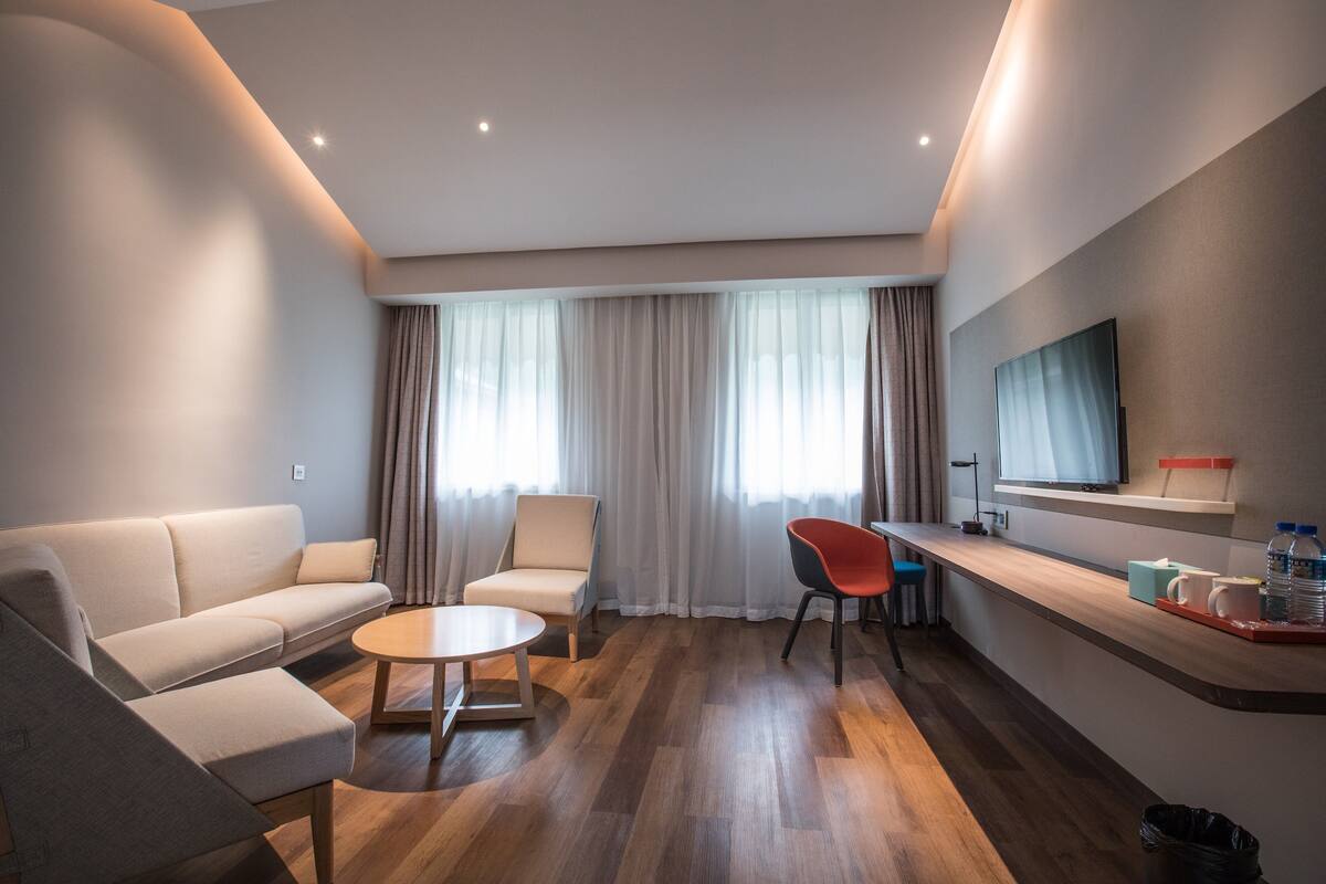 Ein modernes Hotelzimmer mit Sofa, Ohrensessel, Couchtisch und einem an der Wand montierten Fernseher.