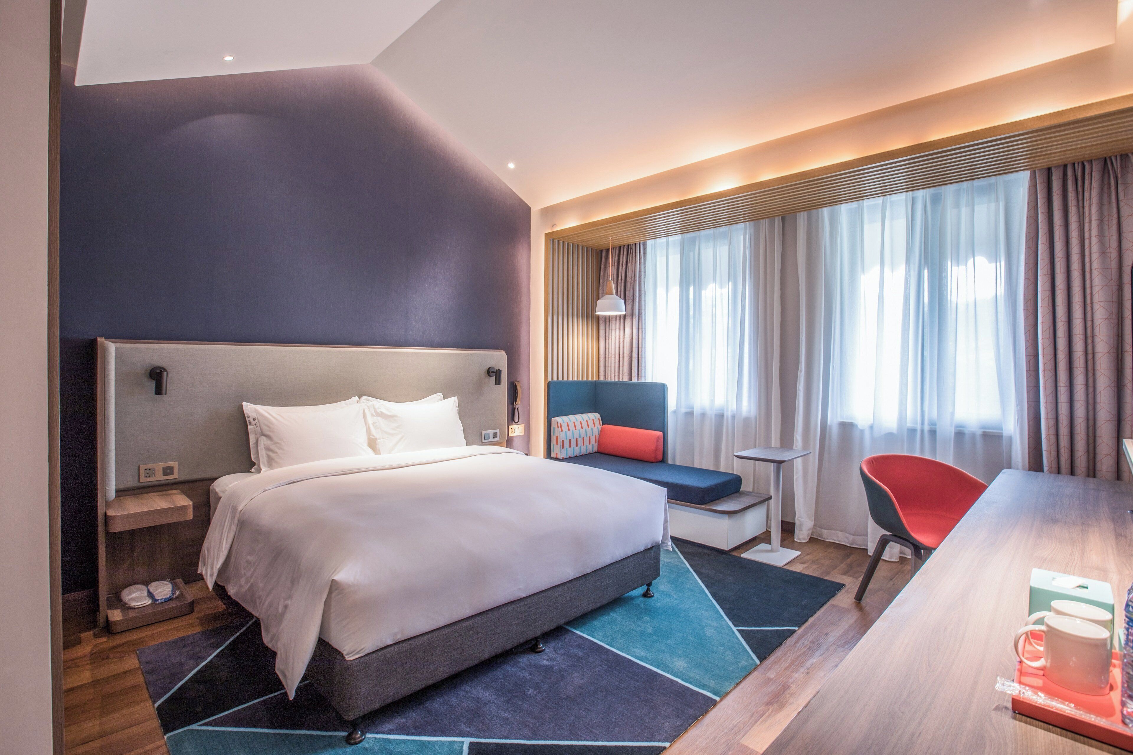 Habitación de hotel moderna con una cama grande, un escritorio, una silla y vistas al exterior a través de la ventana.