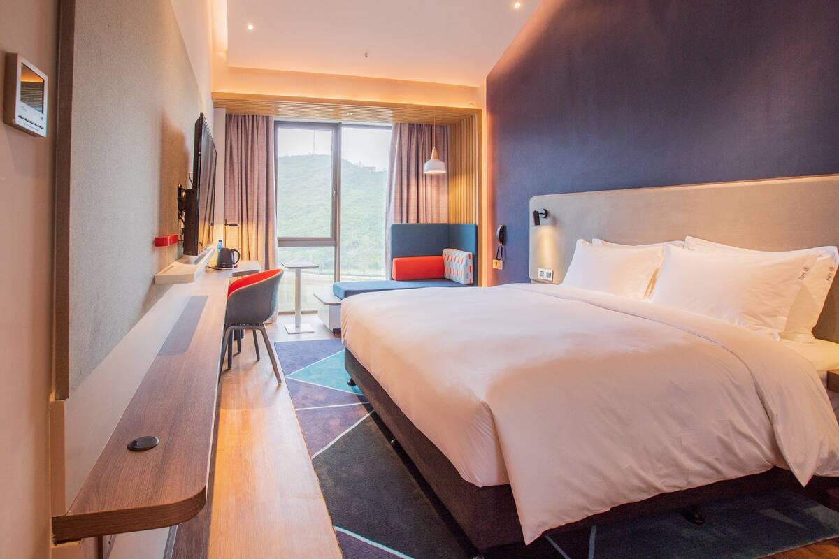 Ein modernes Hotelzimmer mit einem großen Bett, einem Schreibtisch und Blick ins Freie.