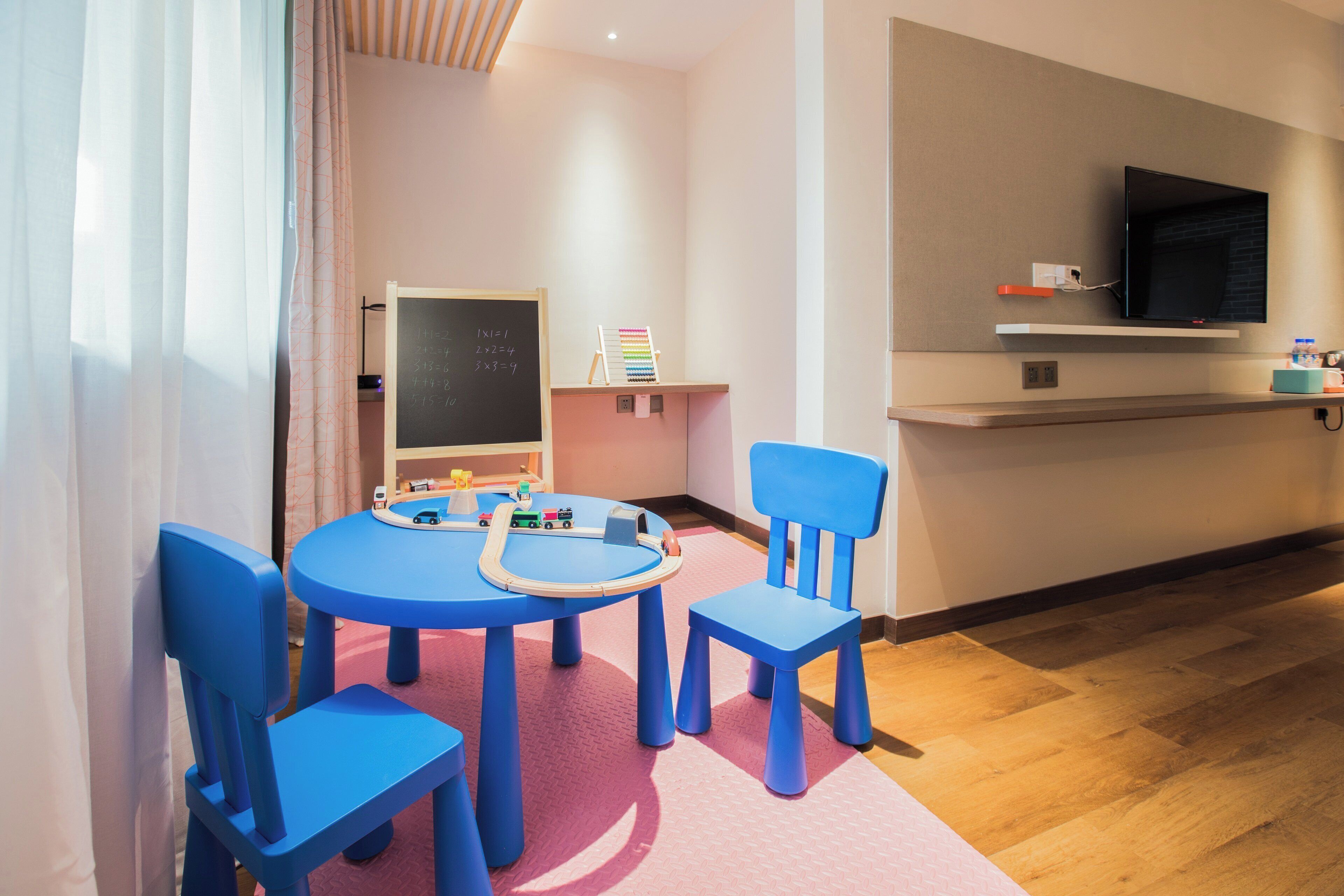 Zona de juegos infantiles con una mesa redonda, sillas azules y un tren de juguete.