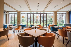 A spacious indoor area with multiple tables and chairs, large windows offering views of the outdoors, and a ceiling with recessed lighting.