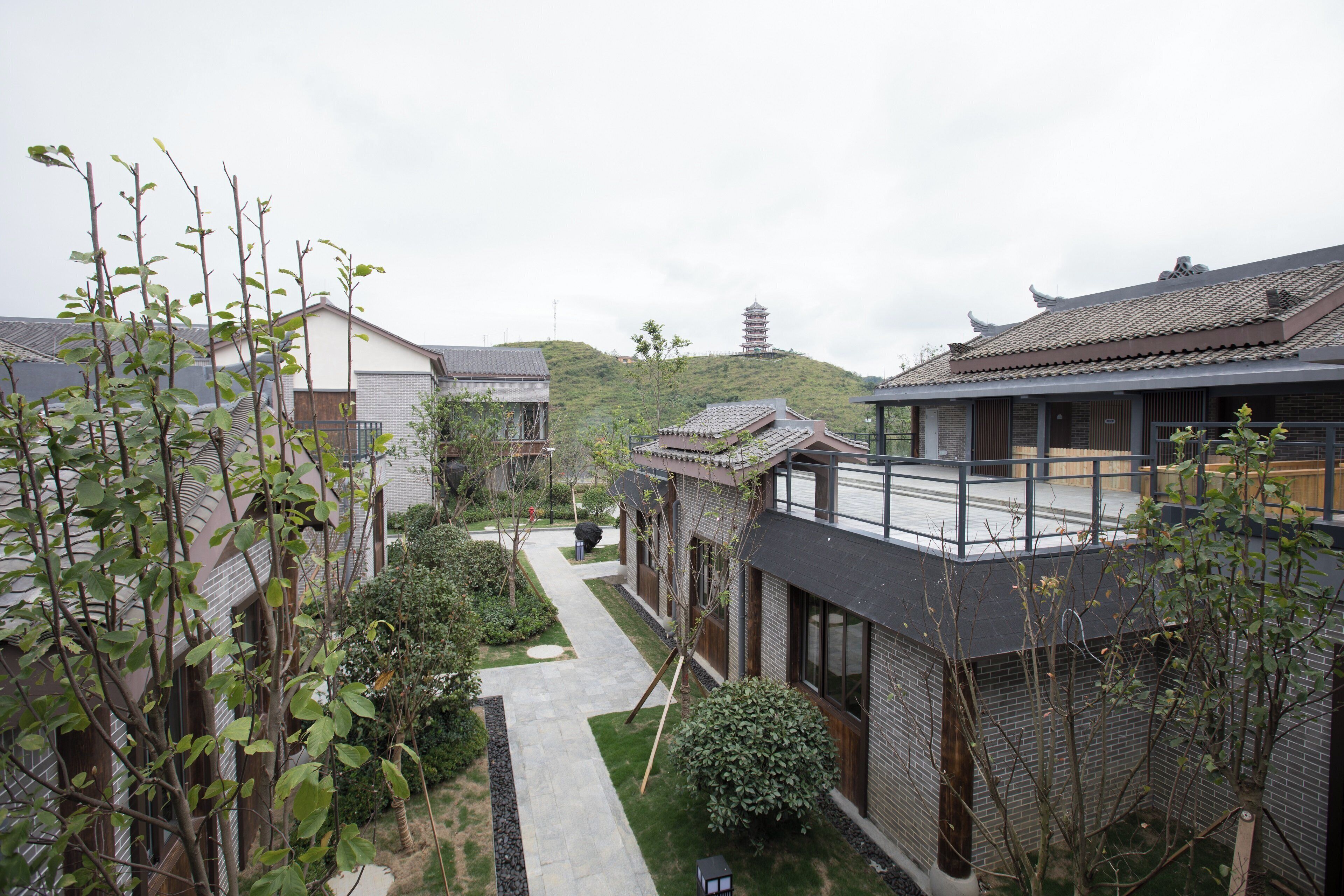 A traditional Japanese-style building with a modern extension, surrounded by greenery and a pathway leading to a pagoda in the distance.