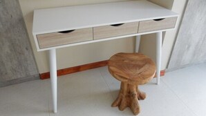 Un bureau blanc doté de deux tiroirs et un tabouret en bois dont le pied est constitué d’une souche d’arbre.