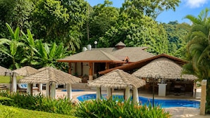 A resort with a swimming pool, thatched-roof structures, and lush greenery. - Hotel Playa Espadilla  (Quepos)