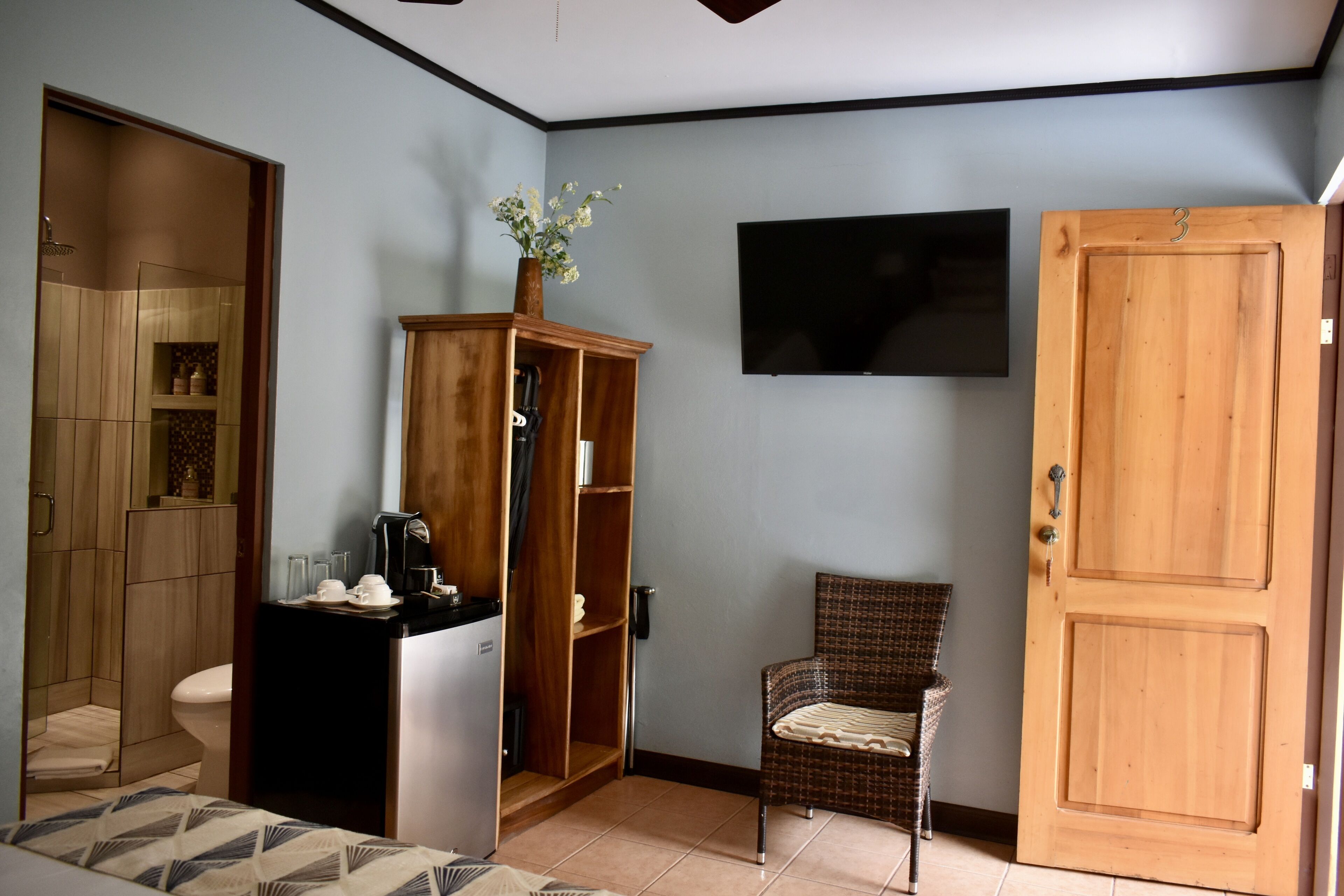 A compact room with a shower, a wooden cabinet, a chair, and a door.