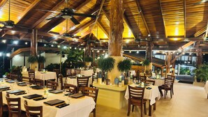 A restaurant with wooden beams, tables set with white tablecloths, and potted plants. - Hotel Playa Espadilla  (Quepos)